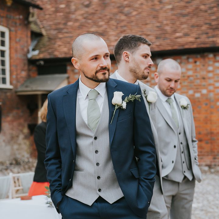 Groom in a dark blue suit with a white rose buttonhole turns to get first look at the bride as she walks down the aisle 
