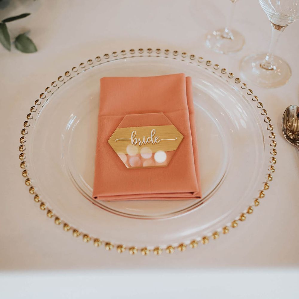 Gold edged clear charger plates with a pink napkin and hexagonal place name 