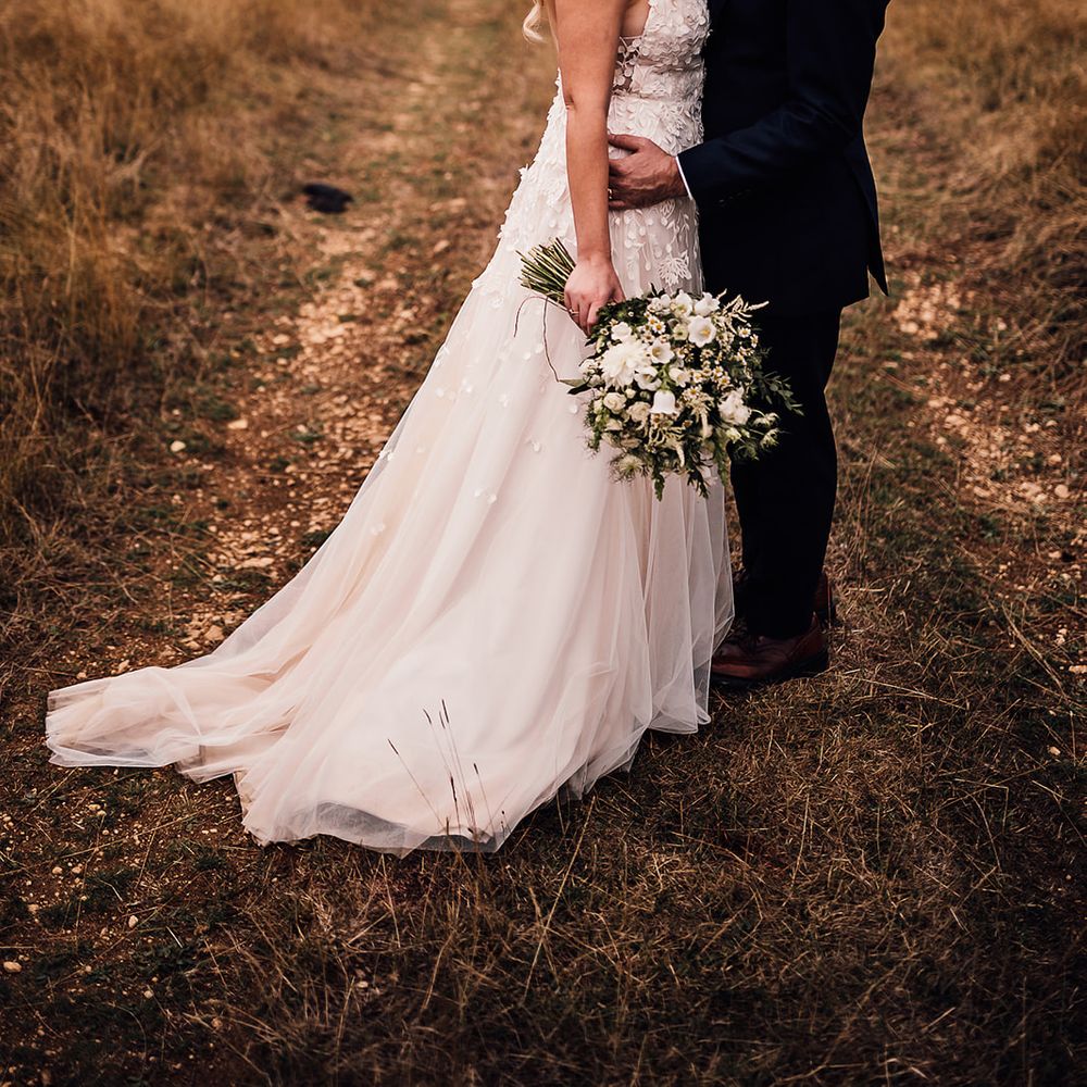 Bride in an applique wedding dress with a short train and pearl headband shares a kiss with the groom in a navy blue suit 