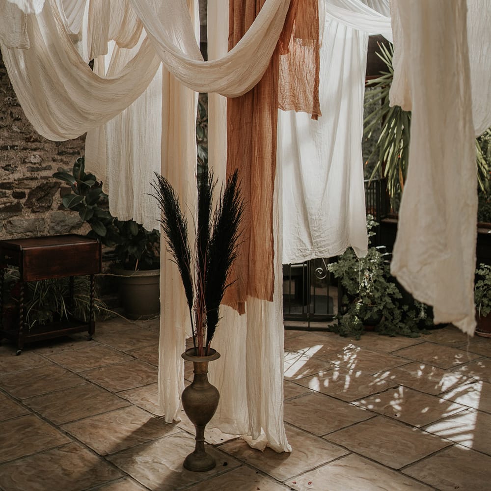White, off white and burnt orange wedding drapes decorations with tropical plants 