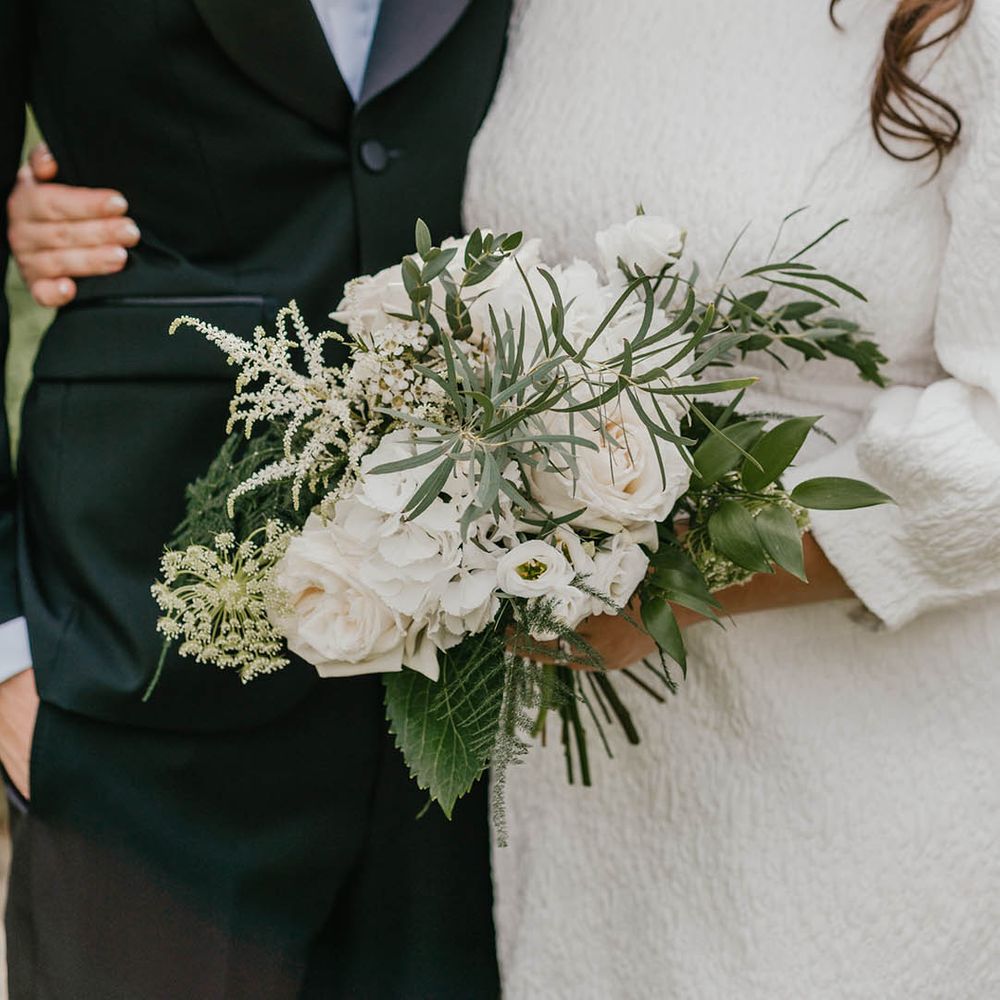 The bride holds an all white flower bouquet with roses and greenery 