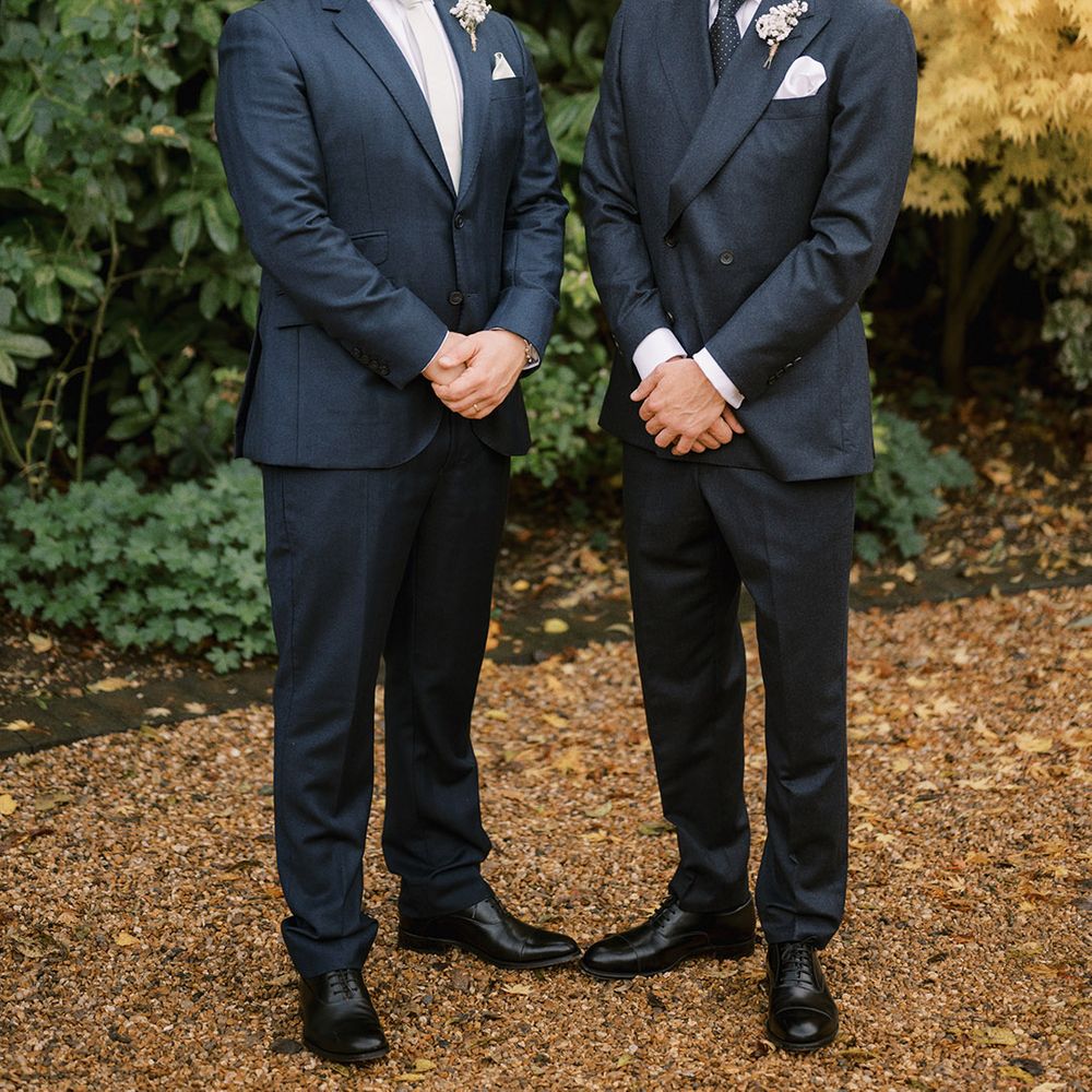 The groom in a dark blue double breasted suit with the best man in a matching colour suit jacket with white baby's breath buttonhole 