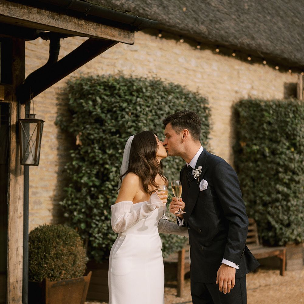 Bride in strapless wedding dress with pearl Jimmy Choo shoes and pearl veil kissing the groom in a dark suit for Oxfordshire wedding at The Tythe Barn