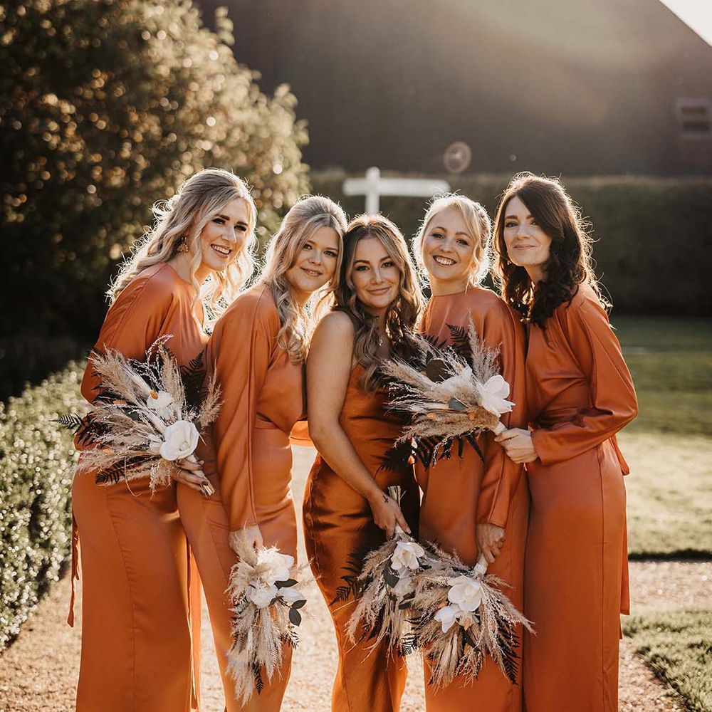 Bridal party wearing mismatched burnt orange bridesmaid dresses holding pampas grass and dried flower bouquets 