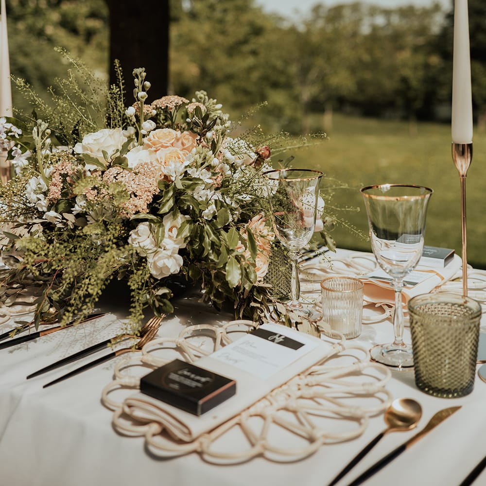 Pink and white flower arrangement decorating the table with white taper candles, a floral wicker placemat and black and white menu card 