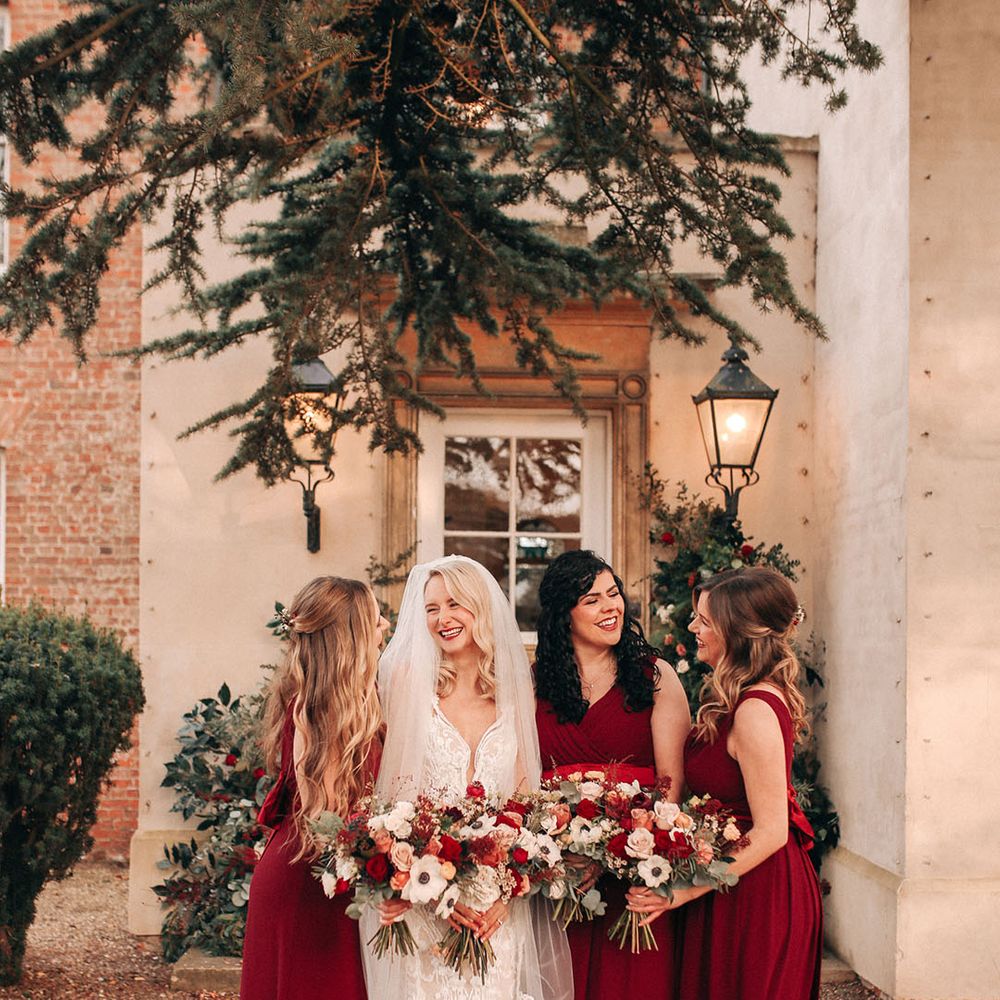 Bridal party wearing festive red bridesmaid dresses with the bride holding red rose bouquets 
