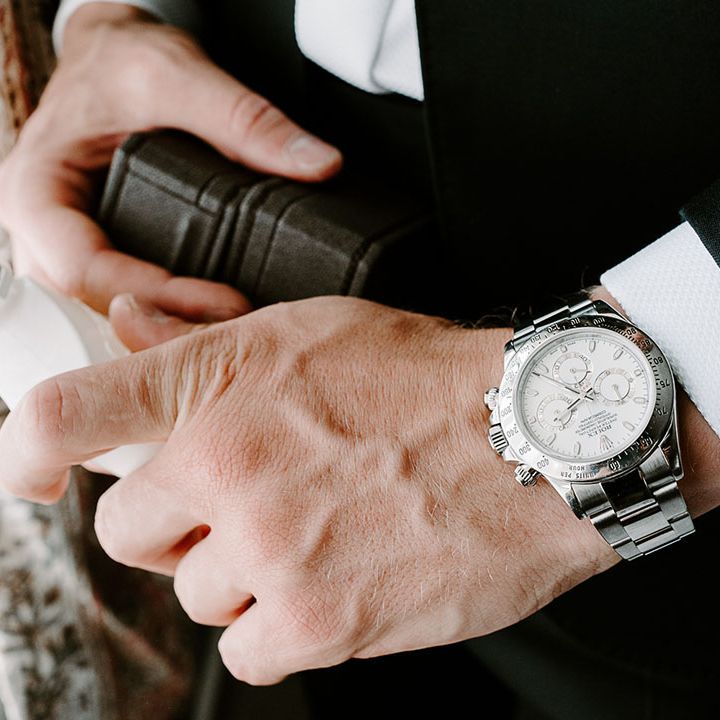 Groom wearing silver watch accessory holding a bottle of Creed cologne 