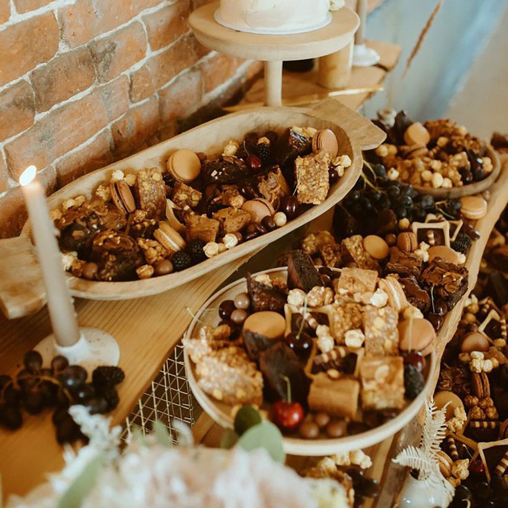 Wedding dessert table with trays of flapjacks, brownies, popcorn, macarons and more with a single tier white iced wedding cake 