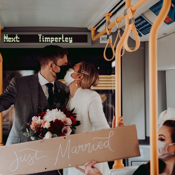 Bride and groom kissing on the tram holding a cardboard 'just married' wedding sign 