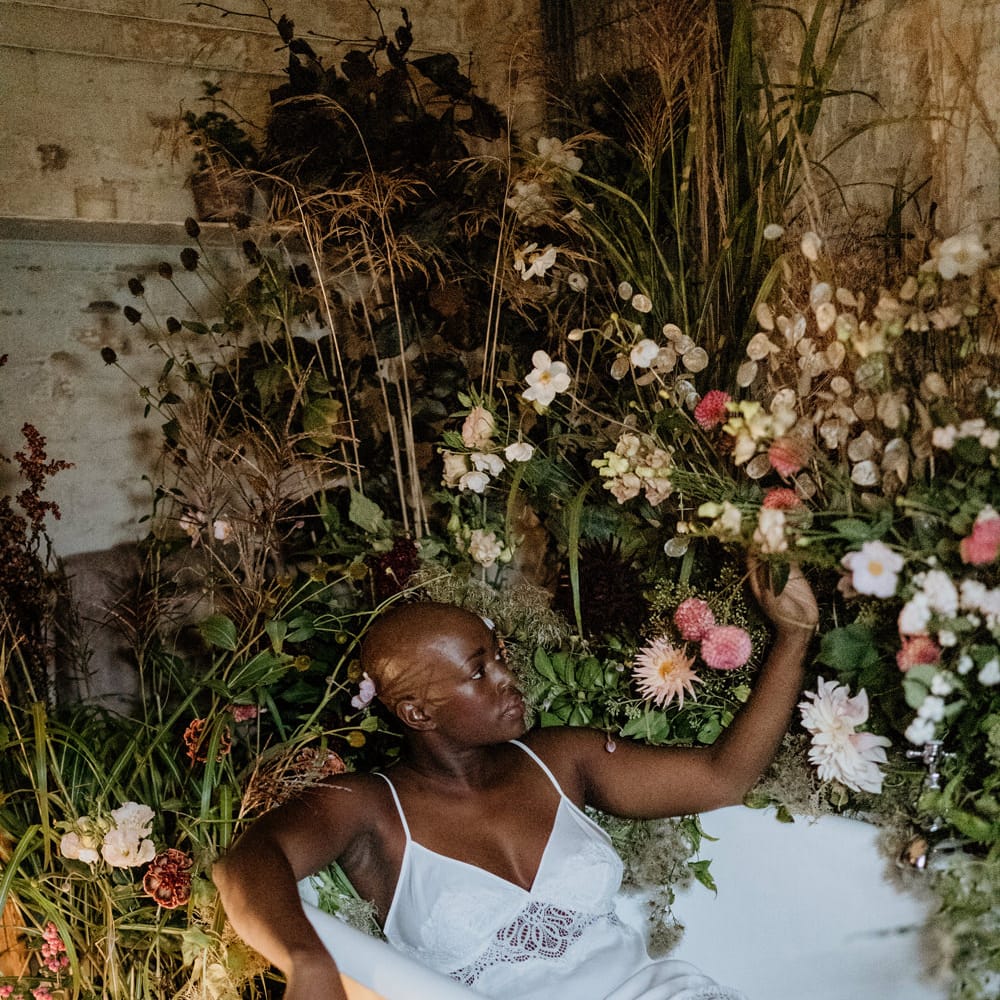 Bride with alopecia in a satin chamise sitting in a roll top bath on the wedding morning 