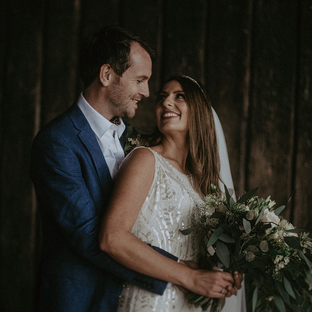 Bride looks back at groom on their wedding day as he embraces her from behind