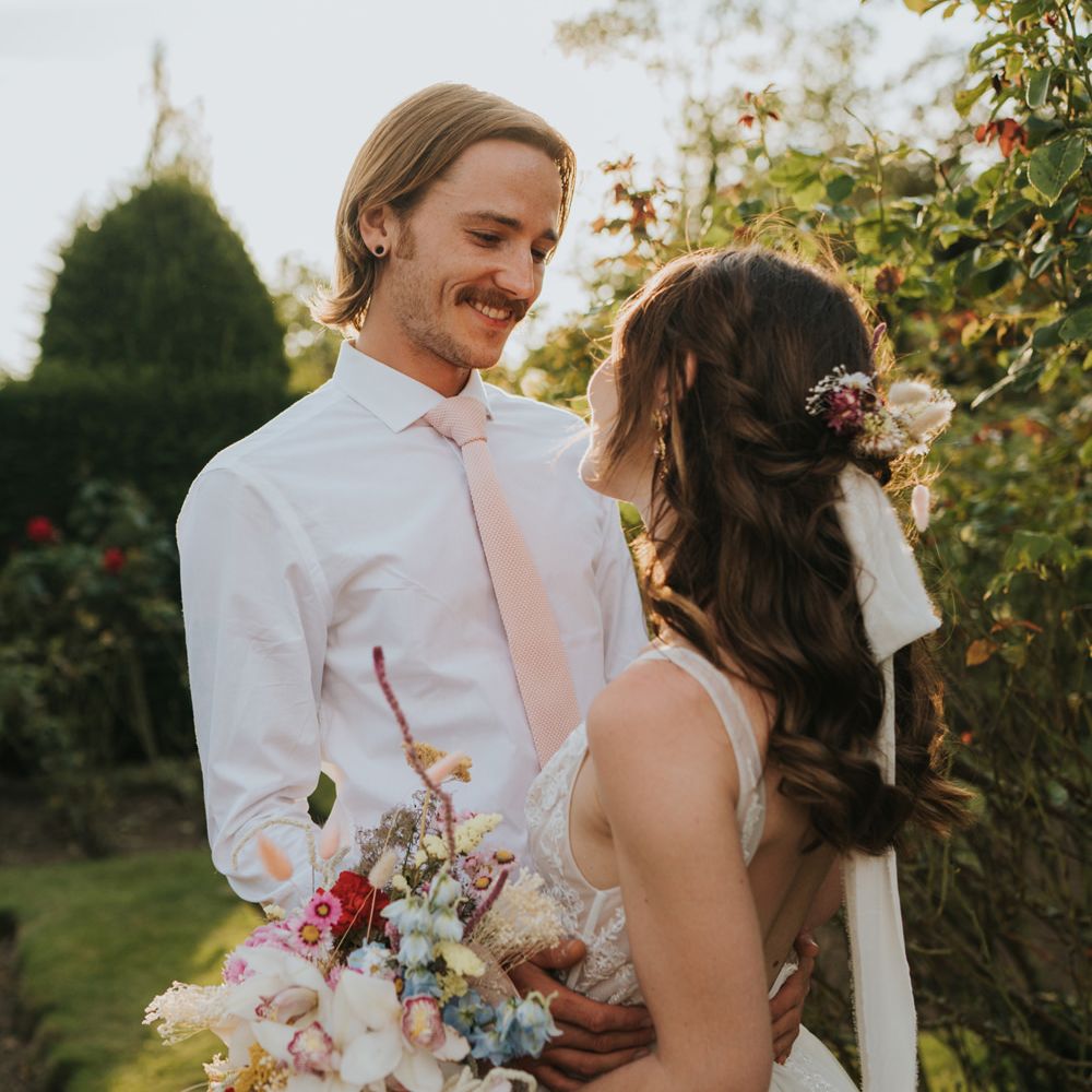 Bride and groom portrait with bride in a Monique lhuillier wedding dress with half up half down hair holding a mixed flower bouquet 