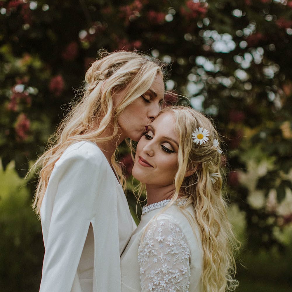 Bride in a wedding cape kissing her bride on the head wearing a long sleeve appliqué wedding dress