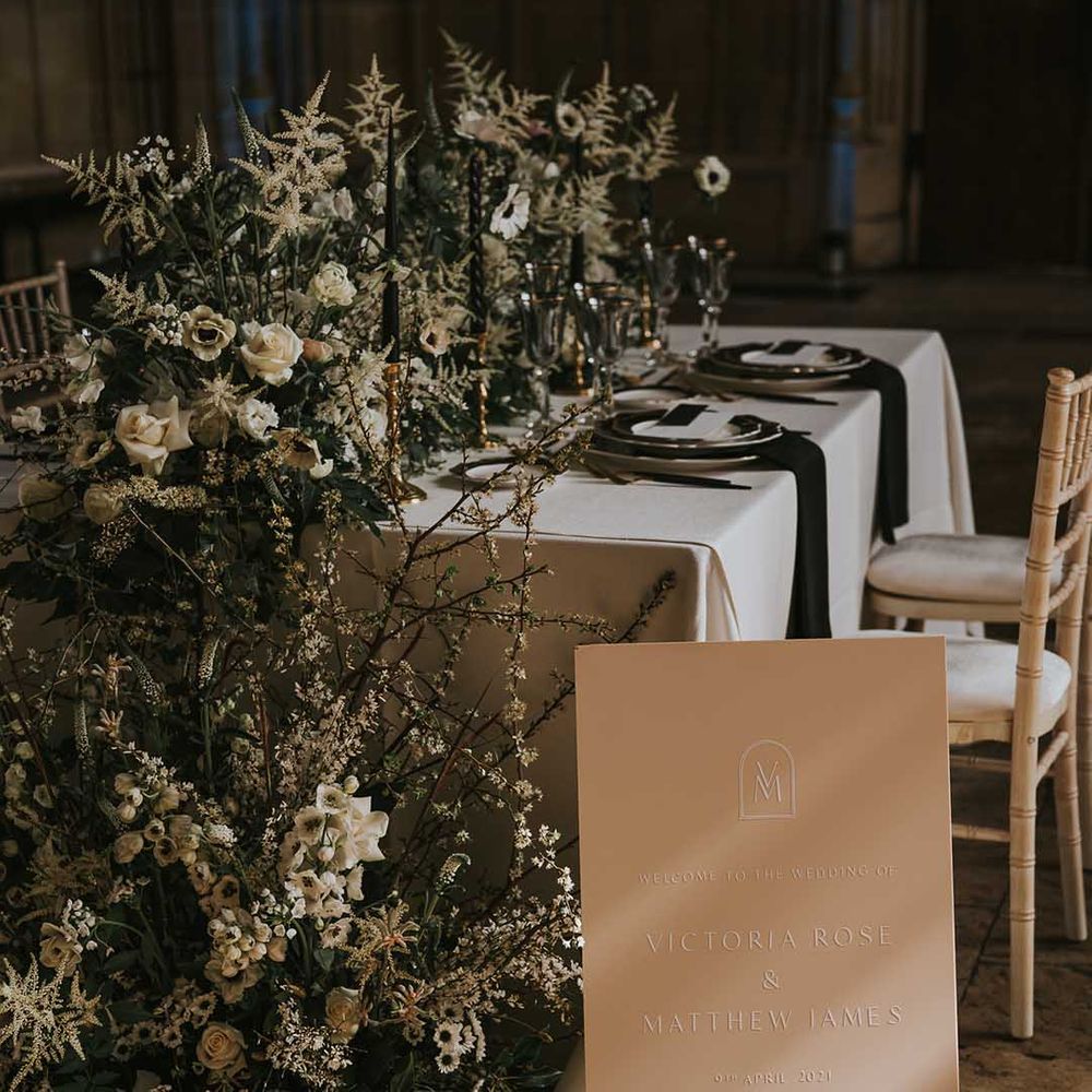 Embossed wedding welcome sign sitting in front of the reception table decorated in white and green flowers 