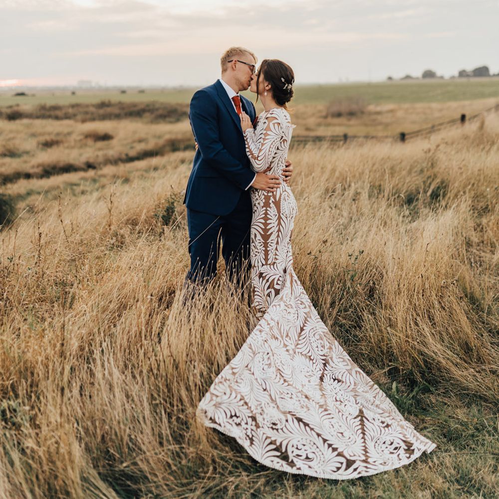 Bride in lace long wedding dress kisses Groom in three piece suit in pampas field 