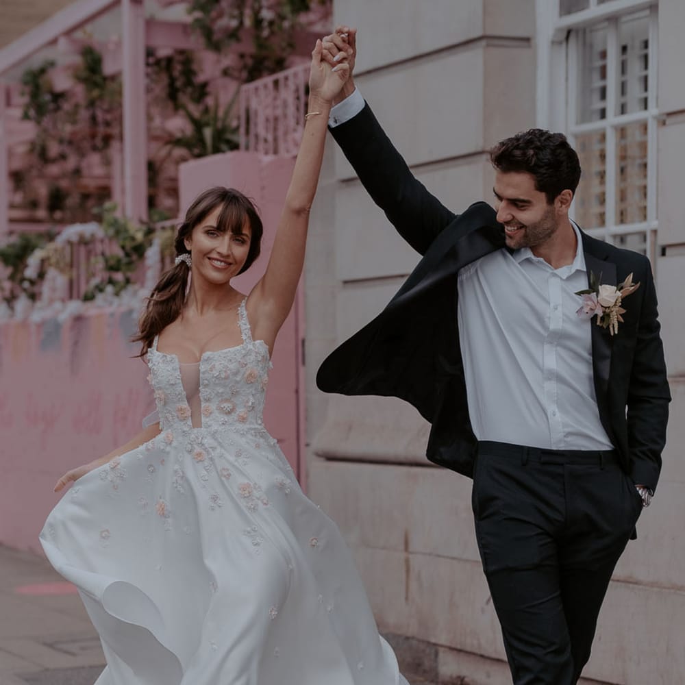 Groom in a black suit and white shirt twirling his bride in a satin and appliqué short wedding dress