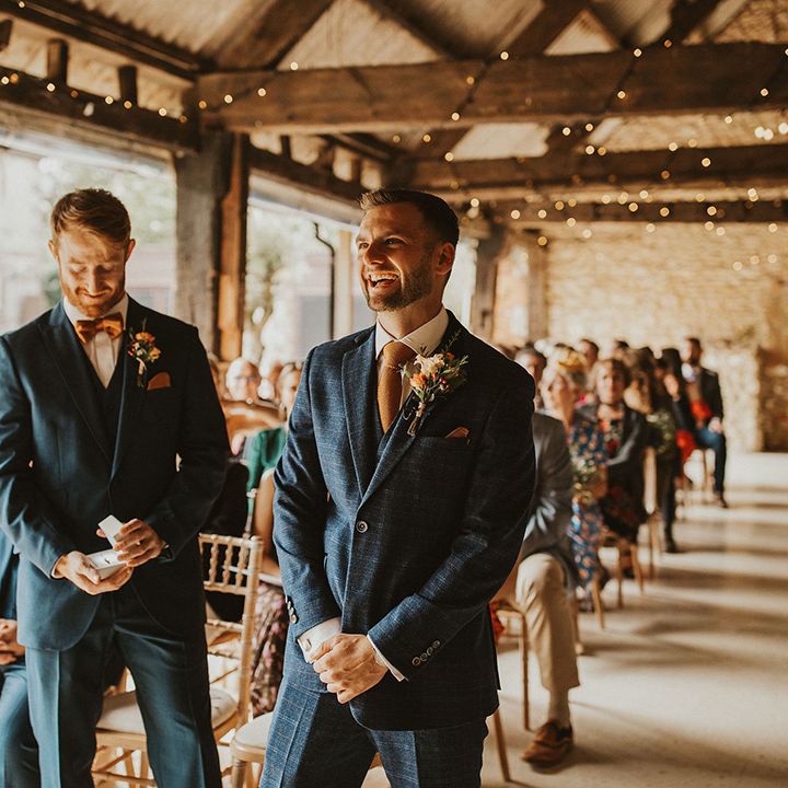 Groom in blue check suit waits for bride at ceremony at East Afton Farmhouse venue