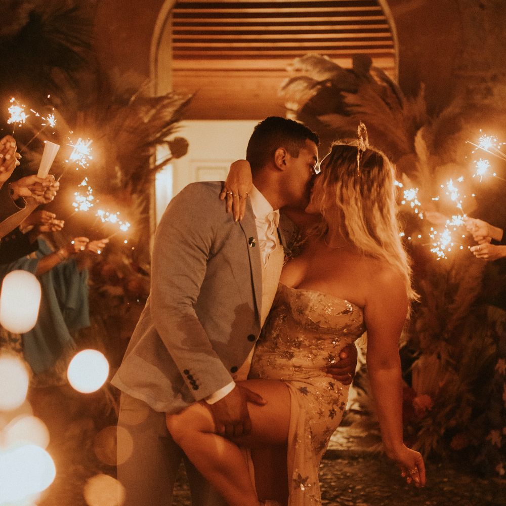 Groom dips back his bride as wedding guests hold sparklers around them
