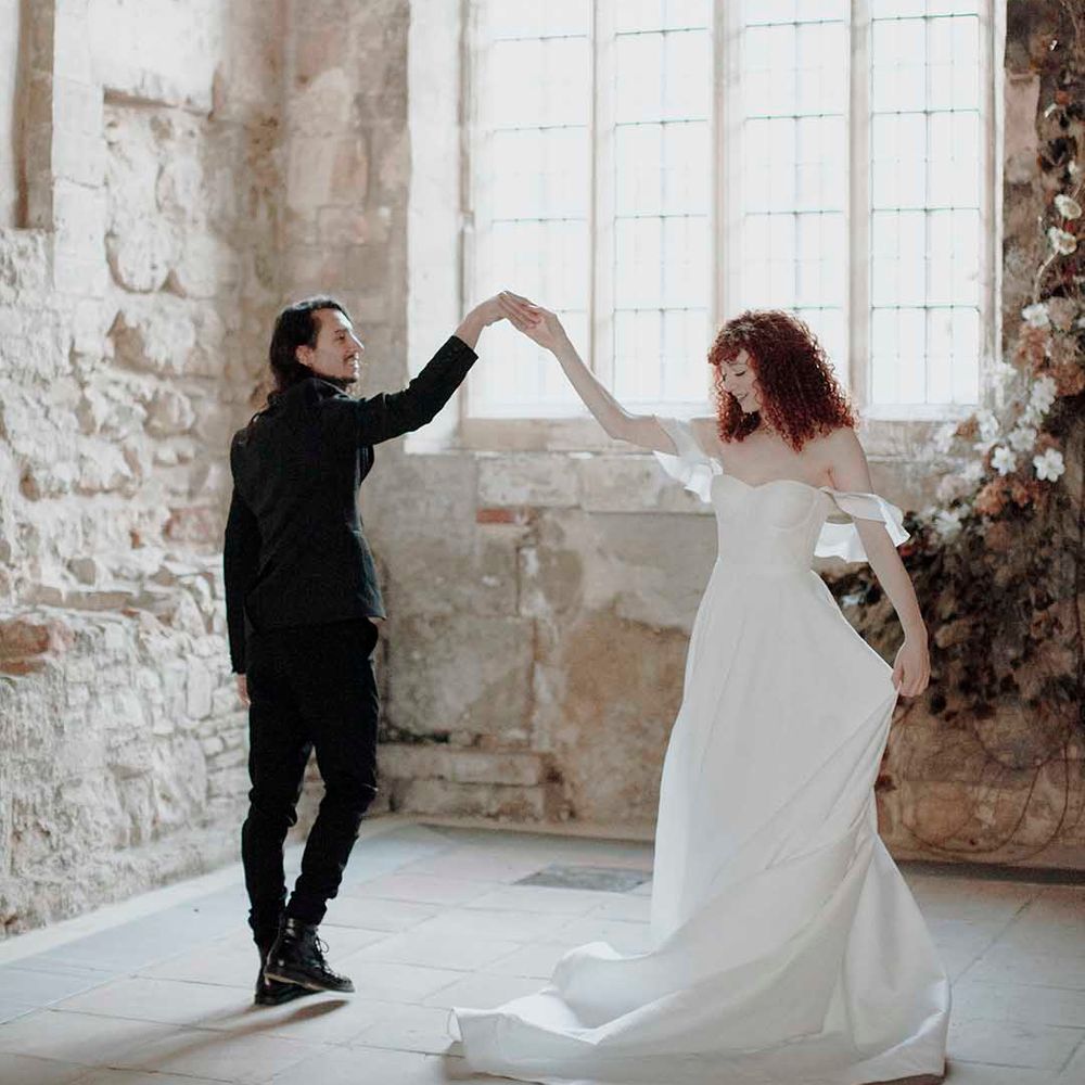 Groom in a black suit with long hair dancing with his bride in a strapless wedding dress with naturally curly hair at the Blackfriars Priory wedding venue 