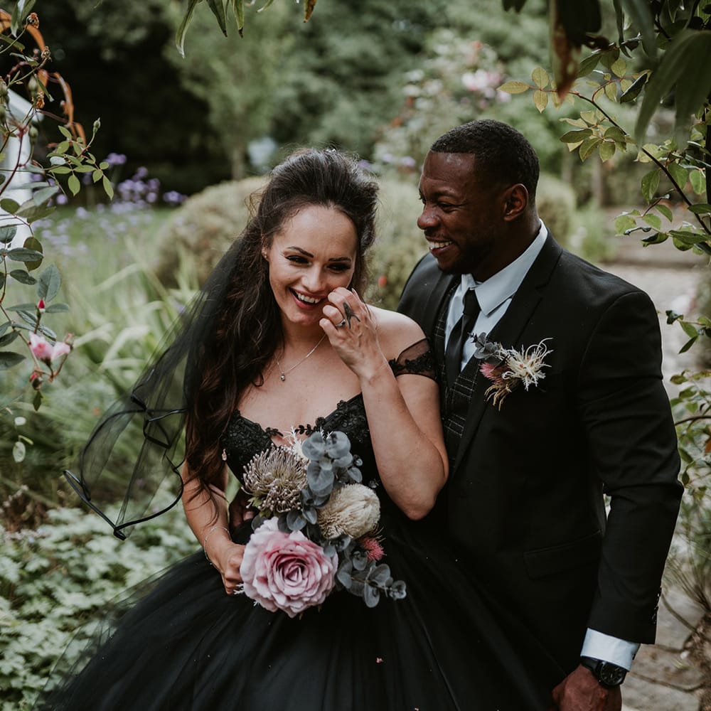 Bride wears black wedding gown whilst holding floral bouquet 