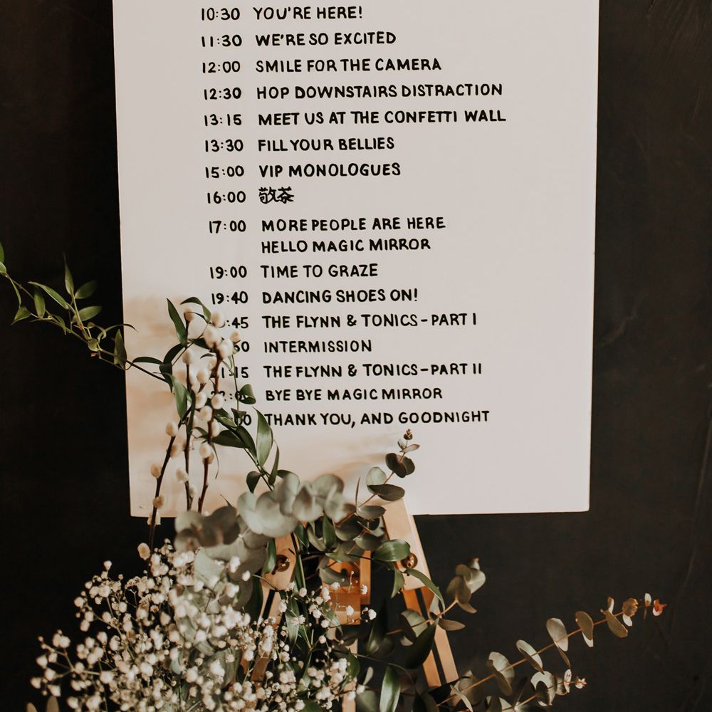 Monochrome wedding order of the day on light wooden easel with foliage decor 