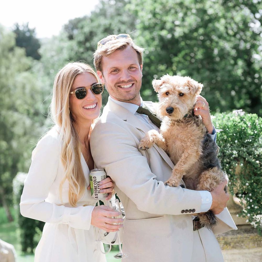 Bride and groom with sunglasses hold their pet dog on their wedding day 