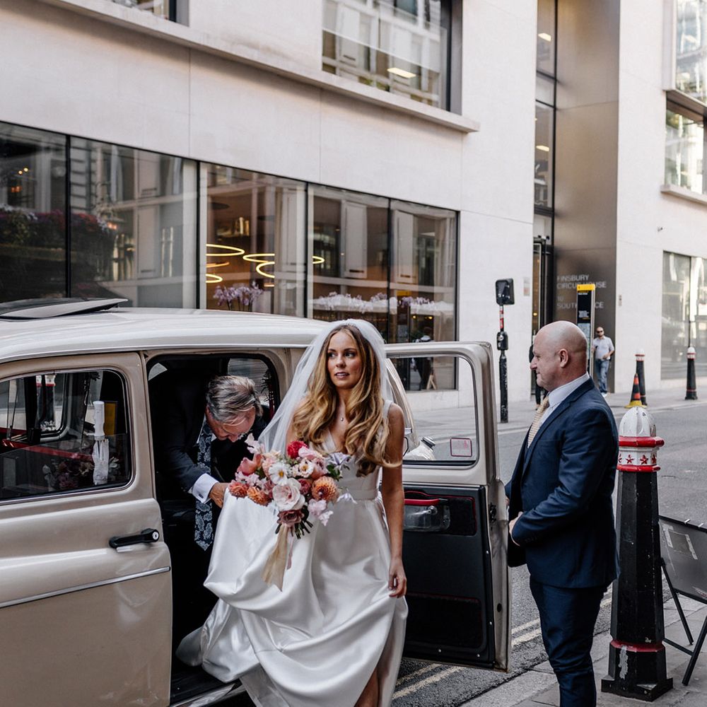Bride in a Karen Willis Holmes wedding dress and silver grey Manolo Blank shoes getting out of a cream London Cab 