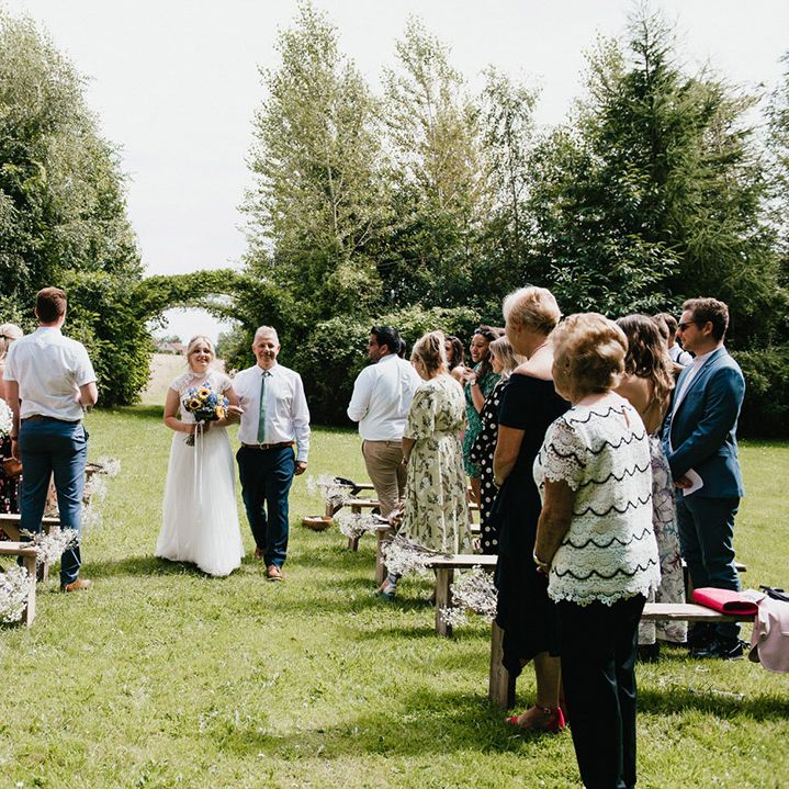 Father of the bride in white shirt and green tie walks bride down the aisle for outdoor ceremony