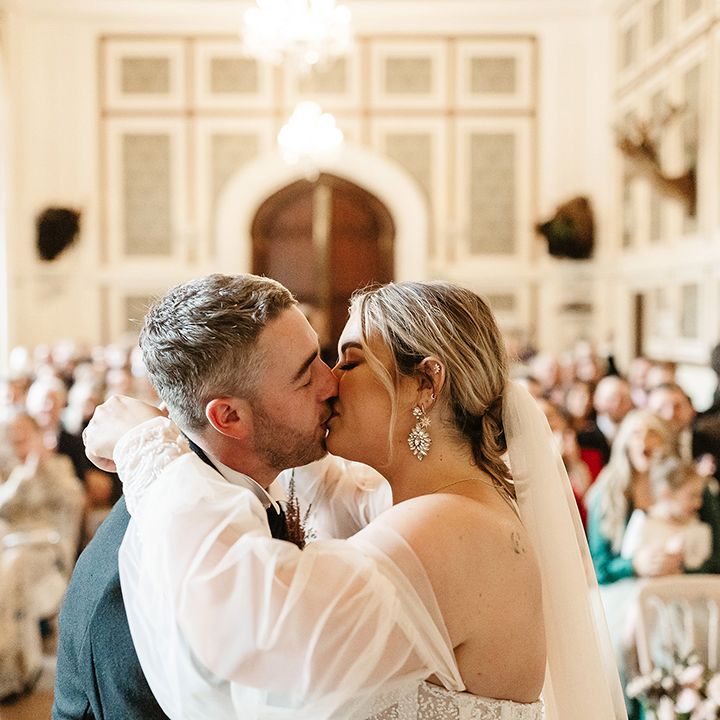 Bride with dangly diamanté earrings has first kiss with groom as a married couple in stunning venue