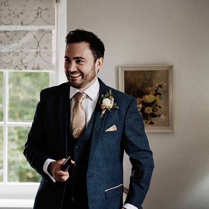 Groom in dark blue suit and gold patterned tie with matching handkerchief and white flower buttonhole