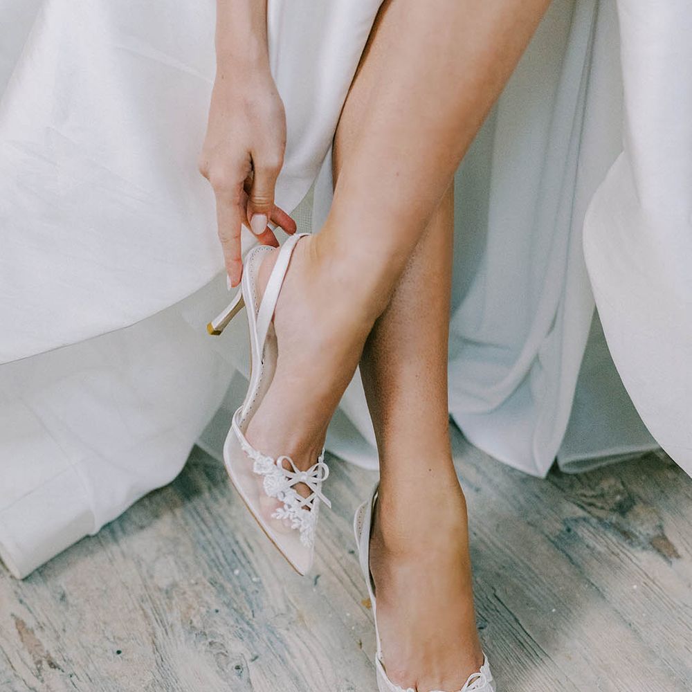 White slingback pointed wedding shoes with sheer lace front with tied white bow ribbon and floral design 