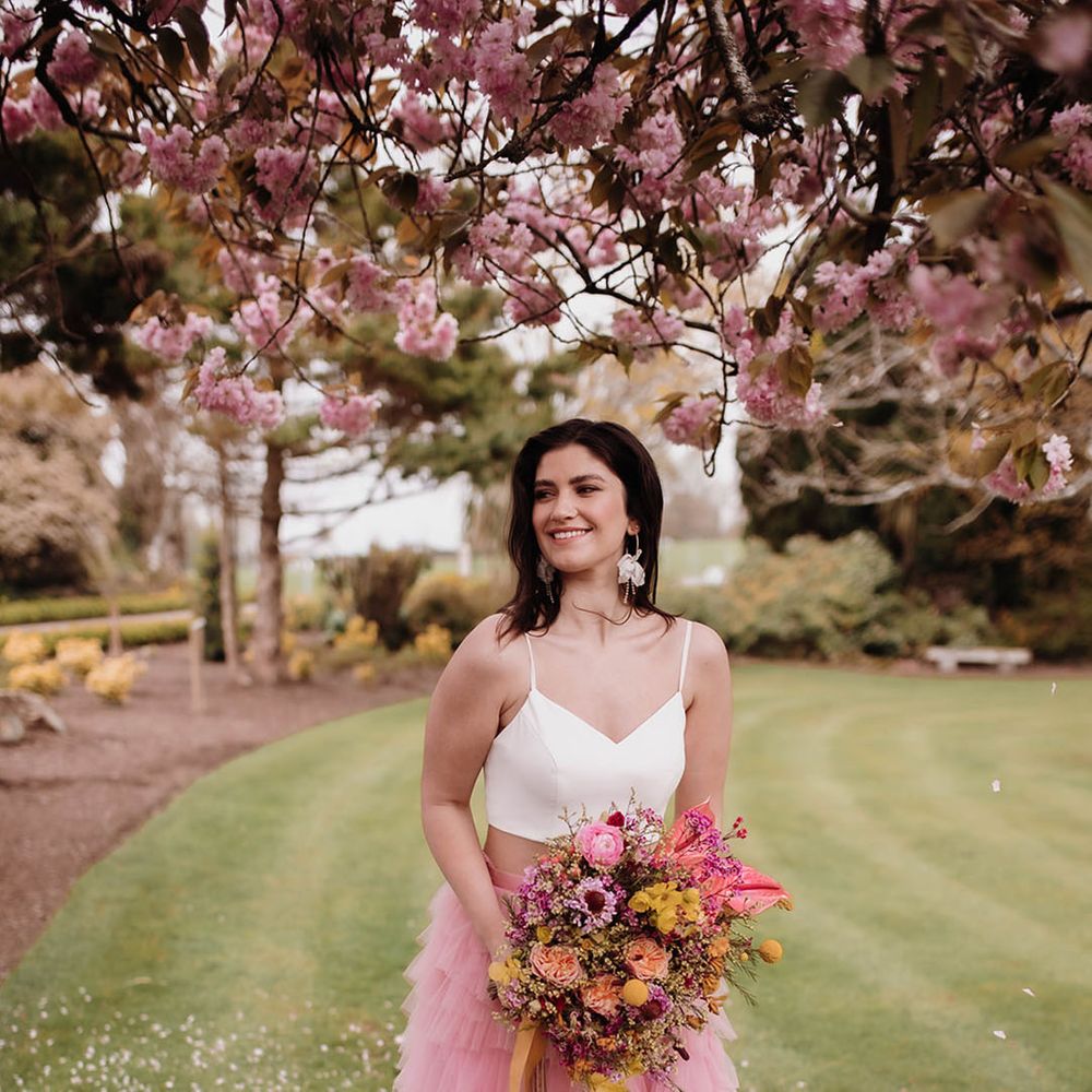 Bride with long wavy hair in a white crop top and layered tulle pink skirt holding a pink and yellow wildflower wedding bouquet 