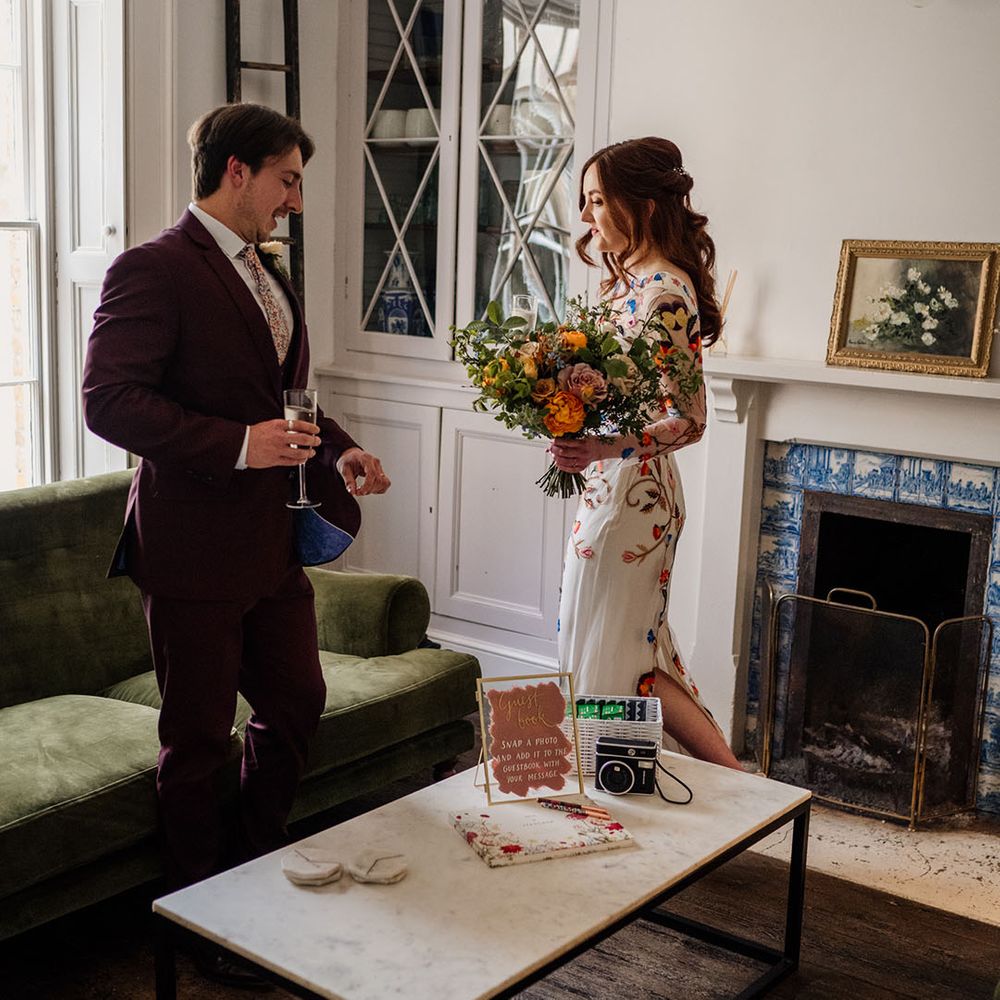 Bride and groom have a glass of champagne together after their ceremony next to table with guest book on 