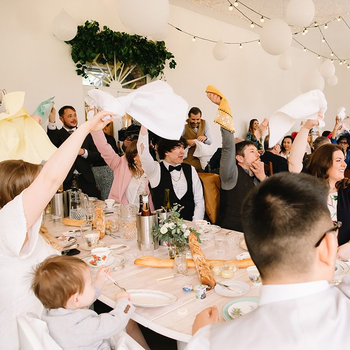 Wedding guests wave their napkins in celebration of the couple with white lantern and fairy light decorations 