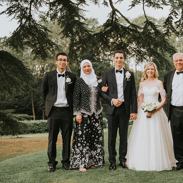 Bride and groom hold hands and pose with the groom's family for classic black tie wedding 