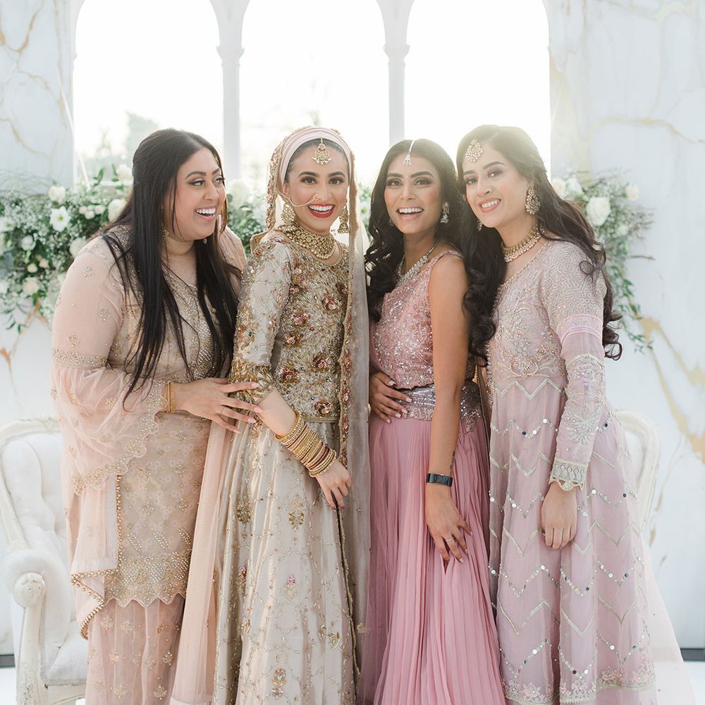 Bride stands with friends who wear pale pink saree's 