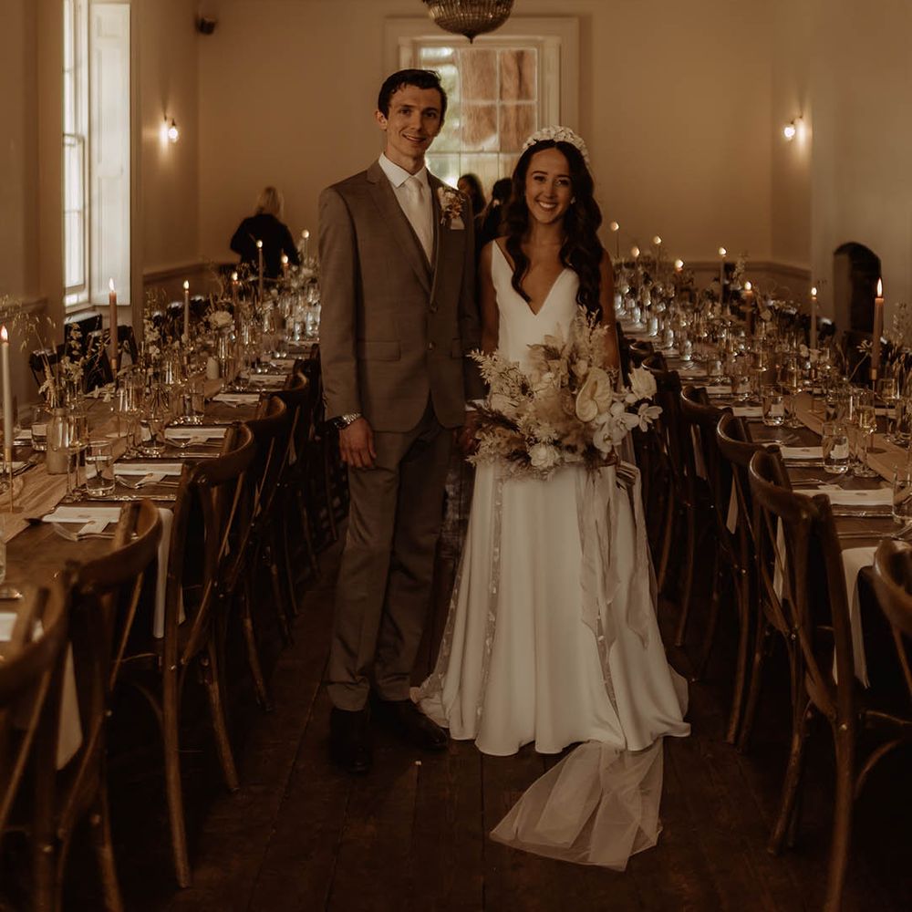 Bride with curled hair in Alexandra Grecco wedding dress with groom in neutral wedding suit smile at the camera