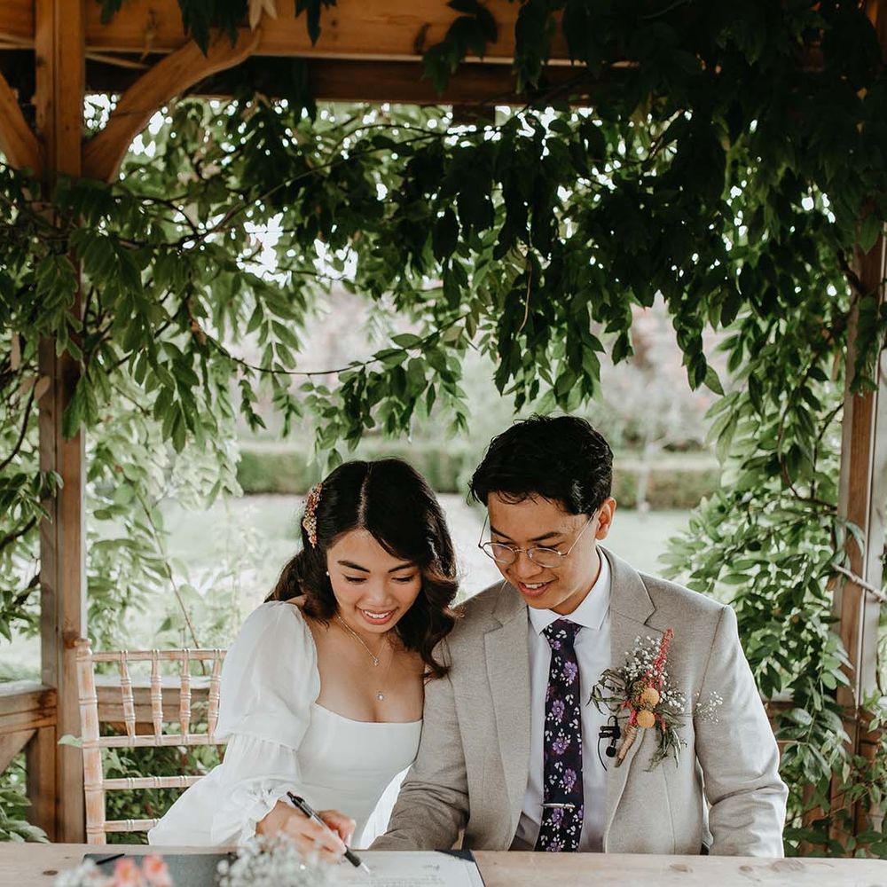 Asian bride and groom signing the resister at their intimate outdoor wedding at The Secret Garden wedding venue 