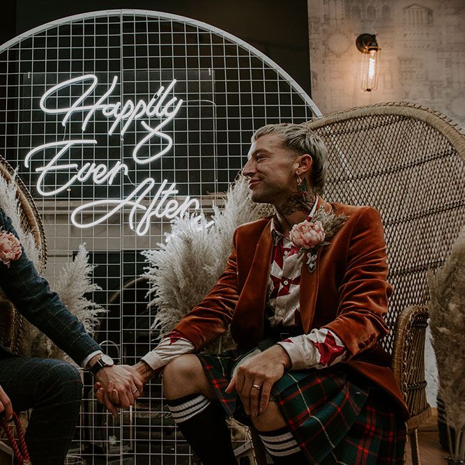 Grooms sit in front of Happily Ever After neon sign 