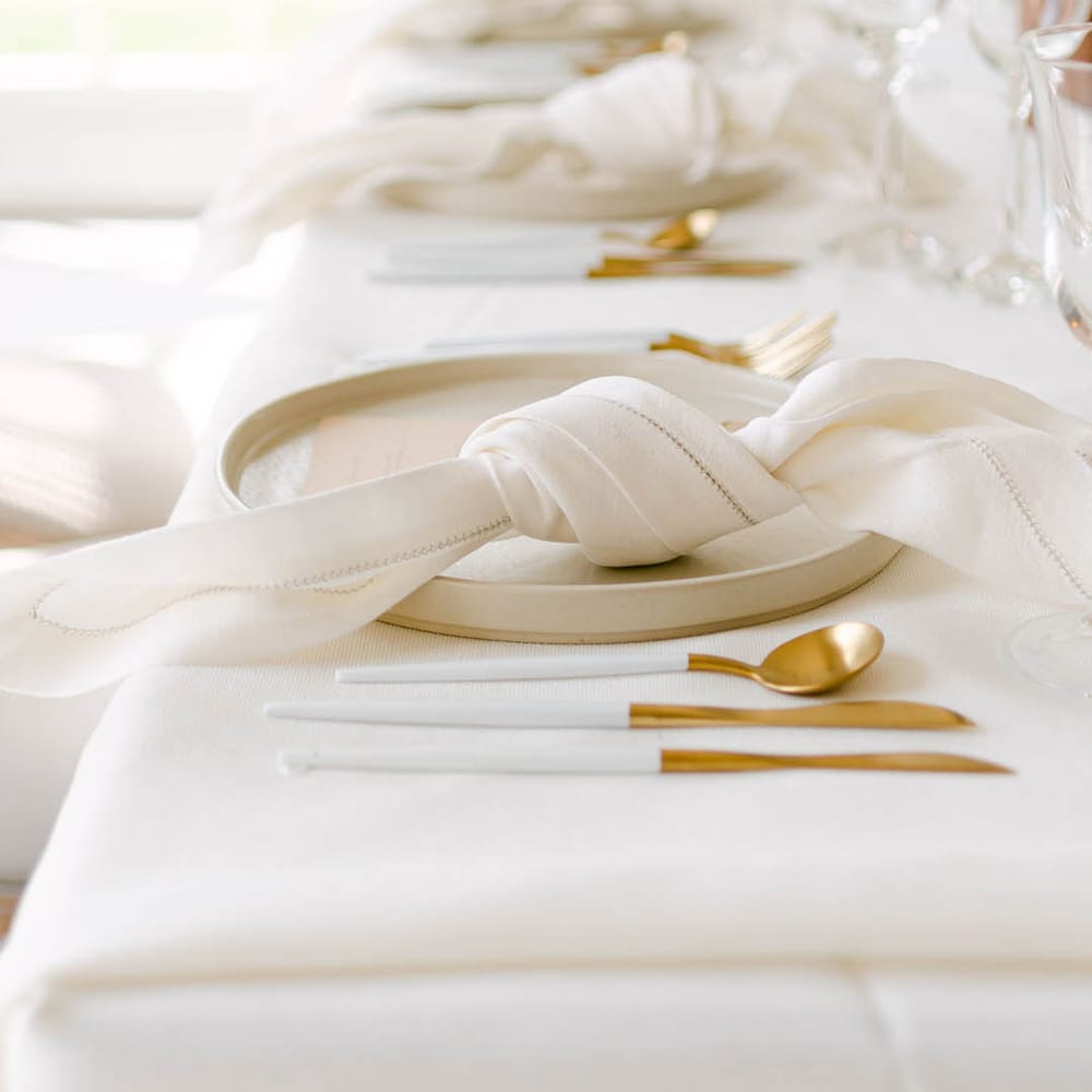 Cream wedding table setting with gold cutlery, ivory napkins and plates for modern and elegant wedding 