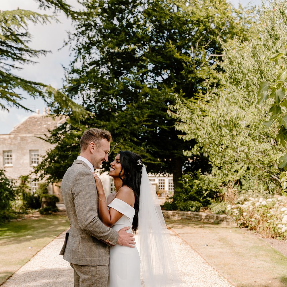 Groom in a brown checkered suit with the bride in an off the shoulder fitted button back wedding dress 