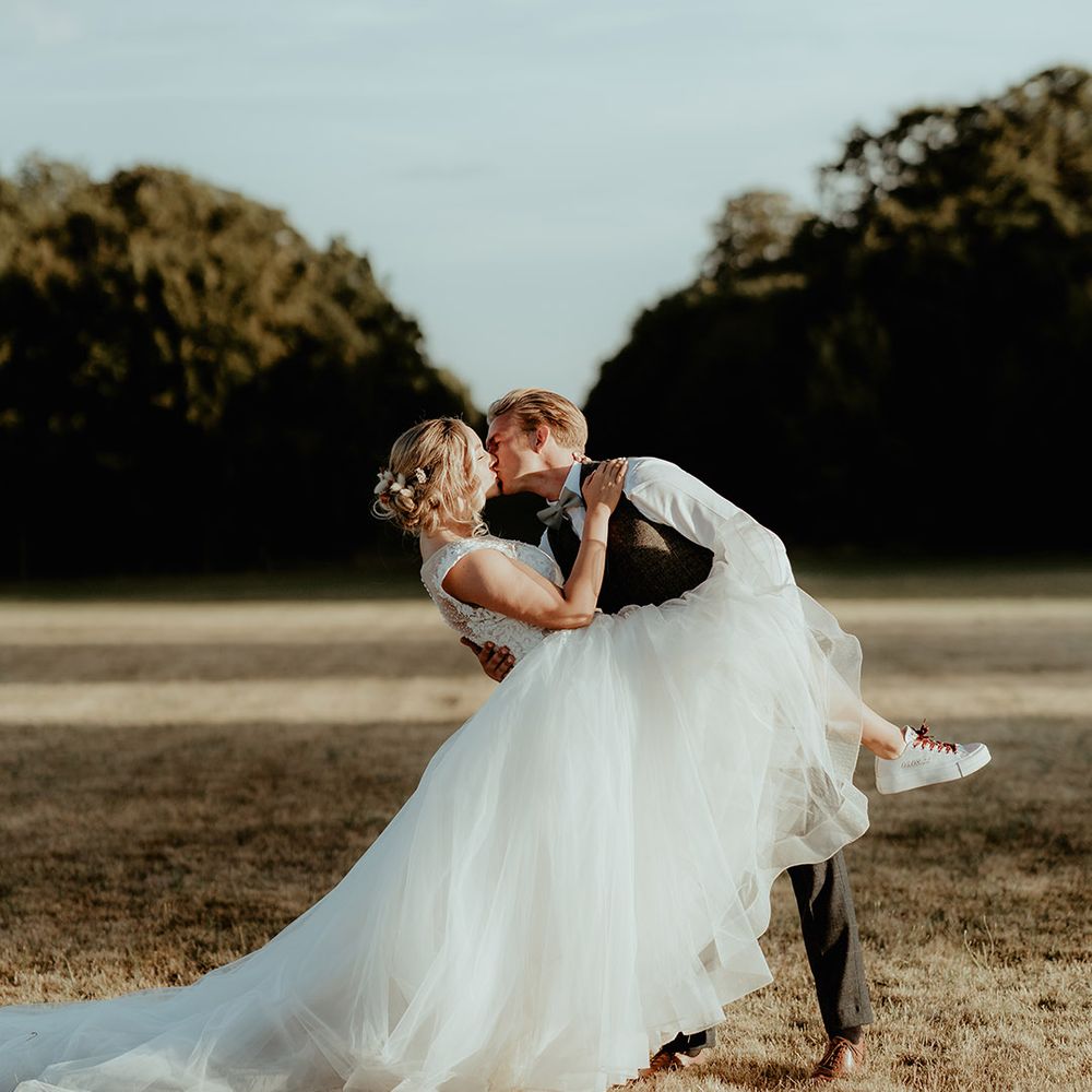 Groom kisses the bride and leans her back as she wears personalised wedding Converses