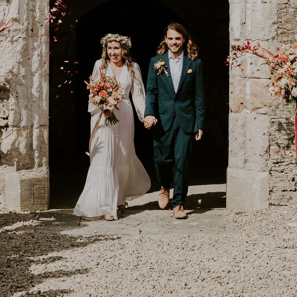 Bride wears floral crown and walks with her groom in green suit after wedding ceremony 