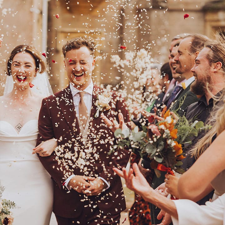 Bride in Vera Wang wedding dress and her groom walk through white confetti after wedding ceremony