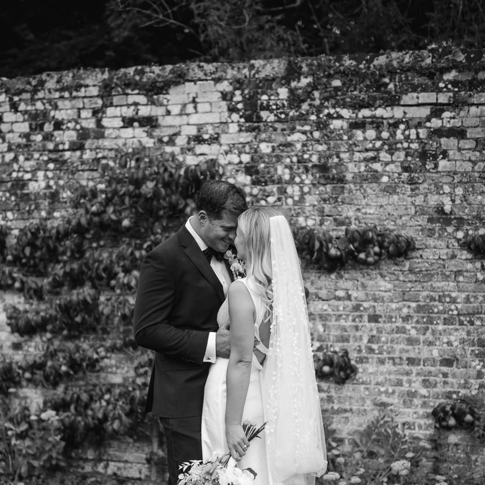 Groom in black tie rests his forehead against the bride who wears a plunging satin wedding dress