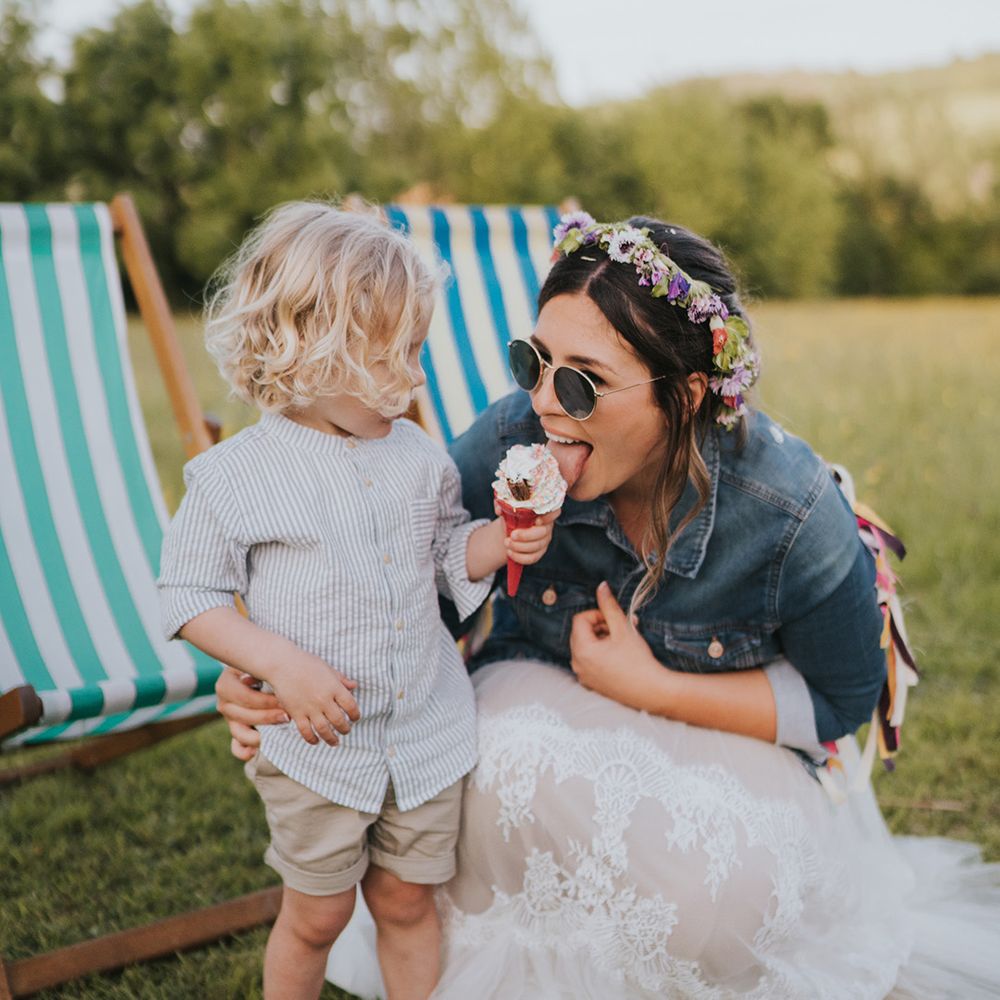 Bride in flower crown and sunglasses eats ice cream with her son 