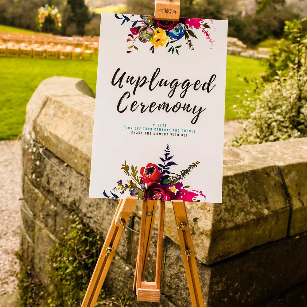 Unplugged wedding ceremony sign on wooden easel complete with colourful floral illustration 