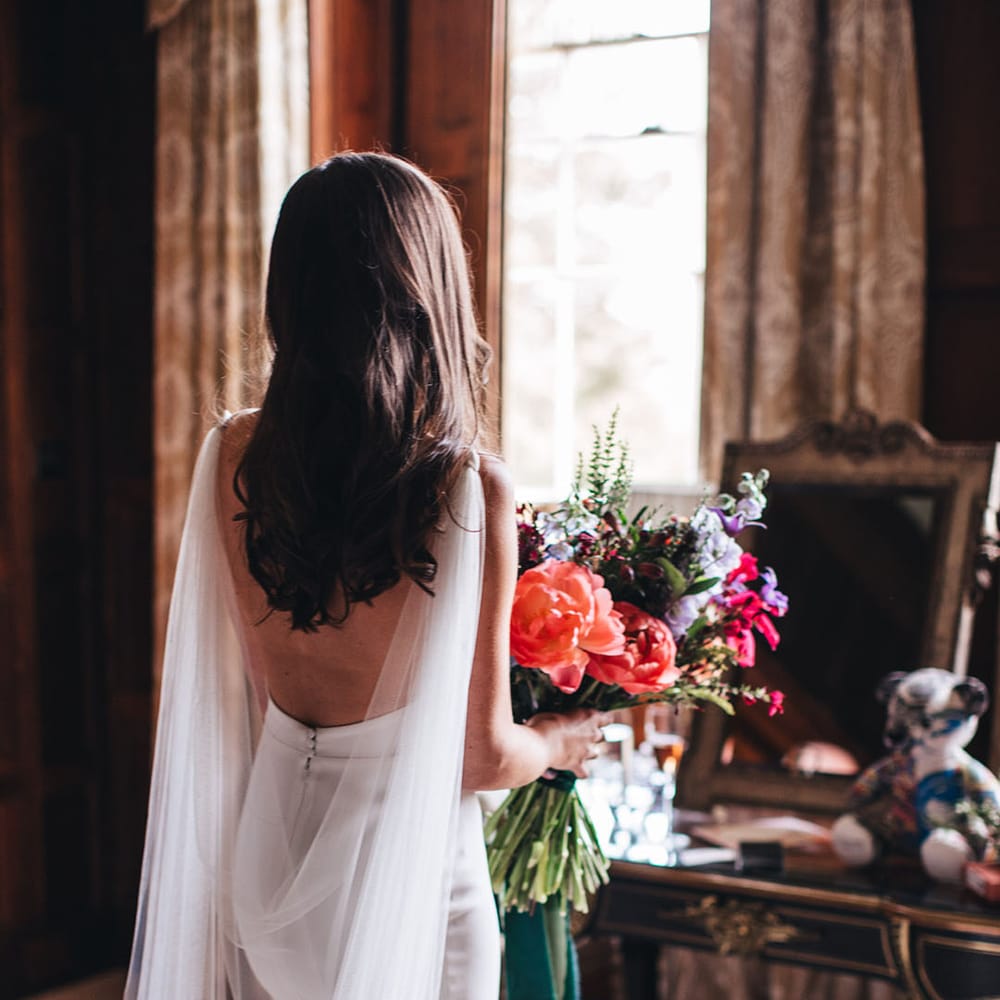 Bride in open back Kyha wedding dress with tulle wings holding a bright pink and red wedding bouquet 