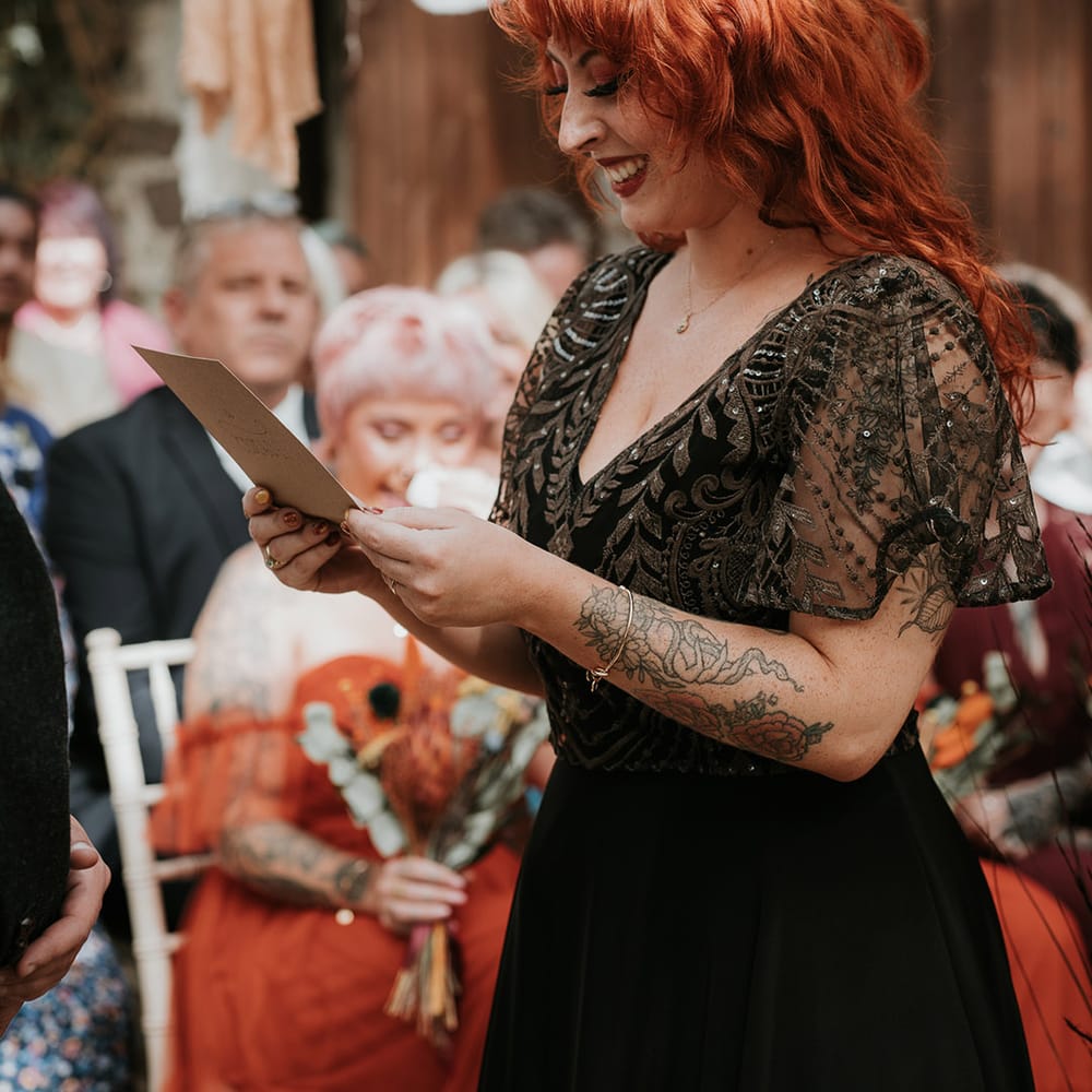 Bride in sparkly embellished v neck black wedding dress doing wedding reading at Westcott Barton, Devon wedding venue 
