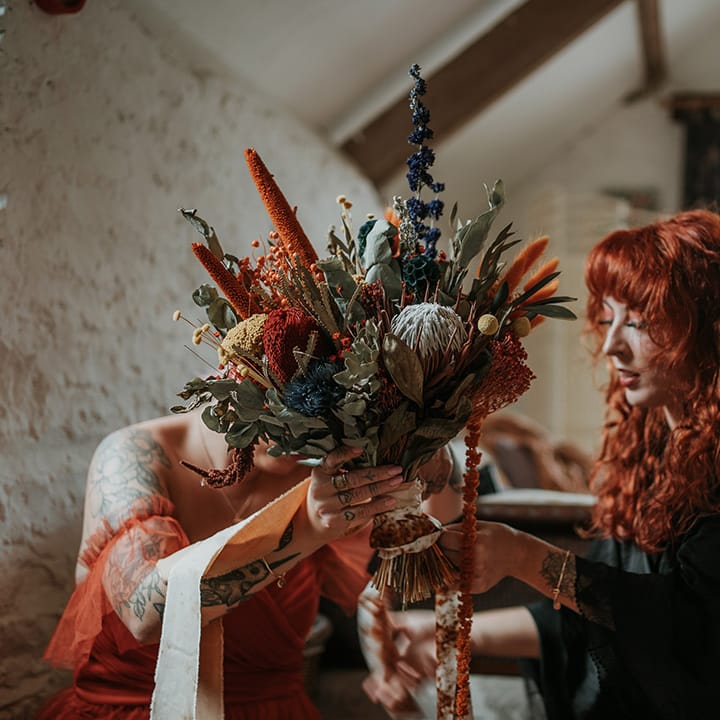 Bride in black wedding dress holding large yellow, blue and orange dried flower bouquet 